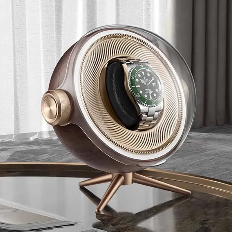 Modern watch winder with gold and wood accents displaying a luxury wristwatch on a table.