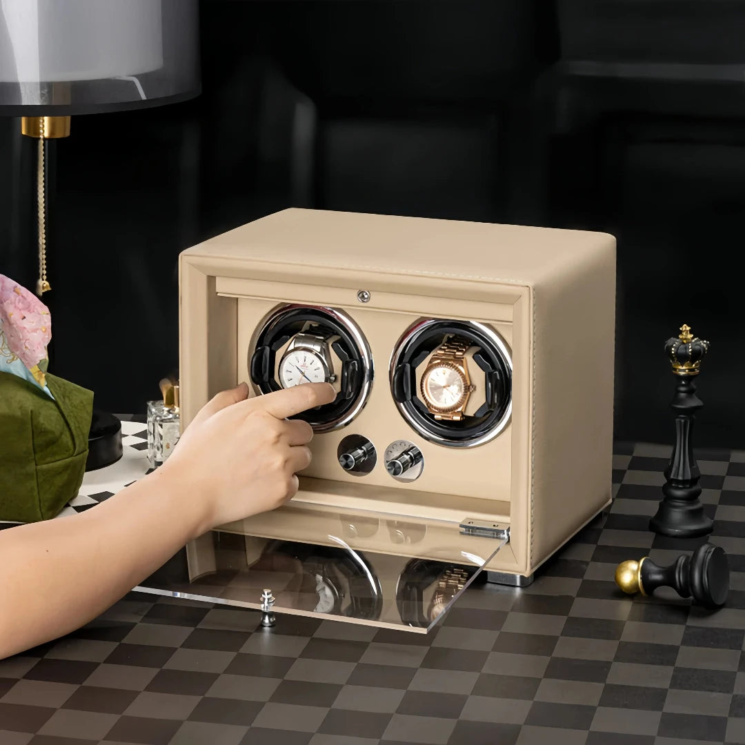 Beige dual watch winder with glass door, holding two watches on a chessboard-patterned table.